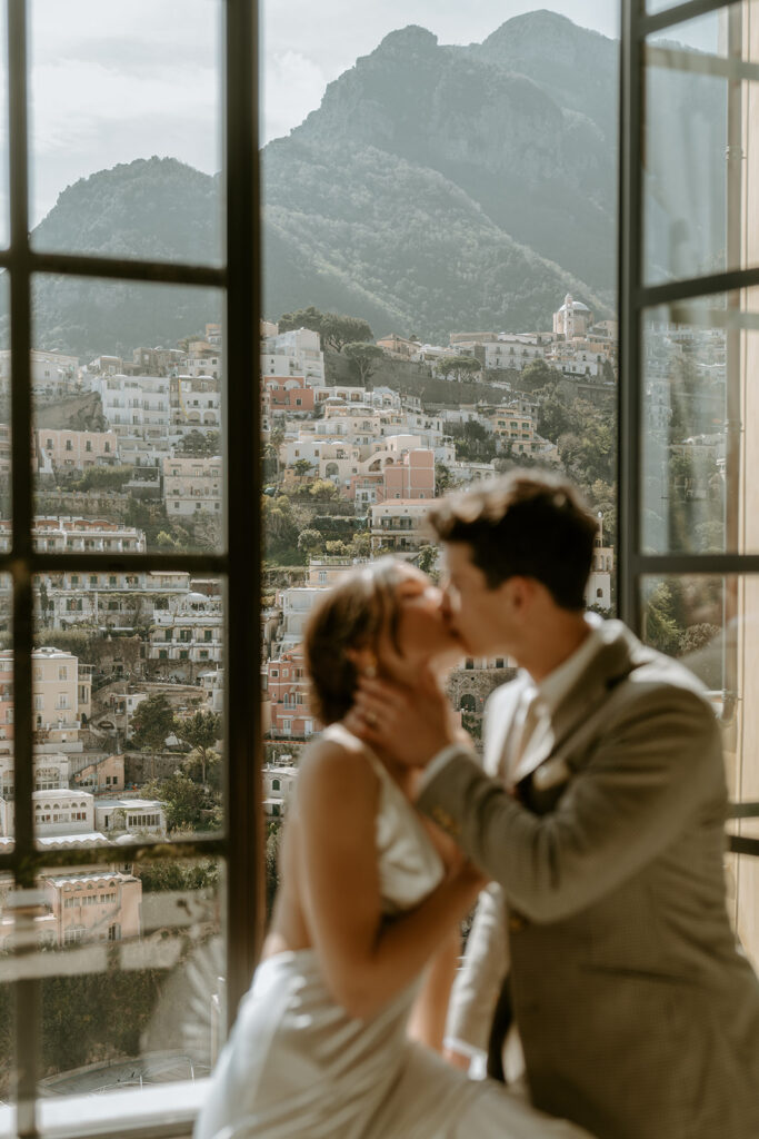 bride and groom kiss on a window sill will Positano in the backdrop