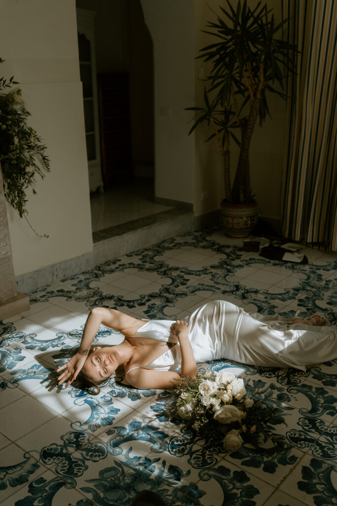 The bride in a silky wedding gown, lying down on the blue printed tiles