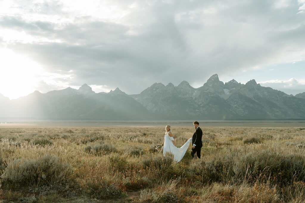 Couple in a vast field with Tetons in the background for their Jackson Hole elopement