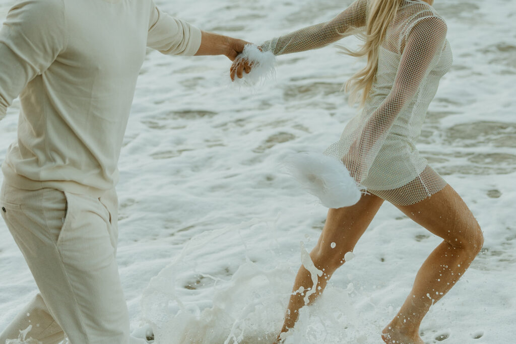 Engaged couple walking along the sandy shore of Malibu Beach during sunrise.